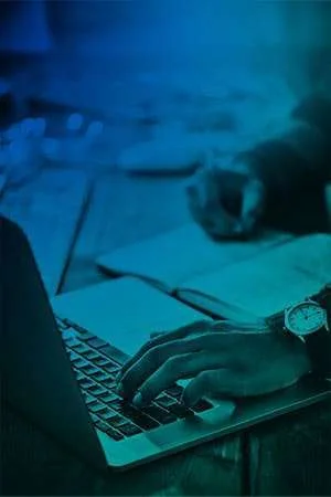 Person typing on laptop, writing notes